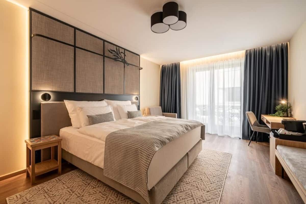 A modern hotel room with a large bed, a desk, and a chair.