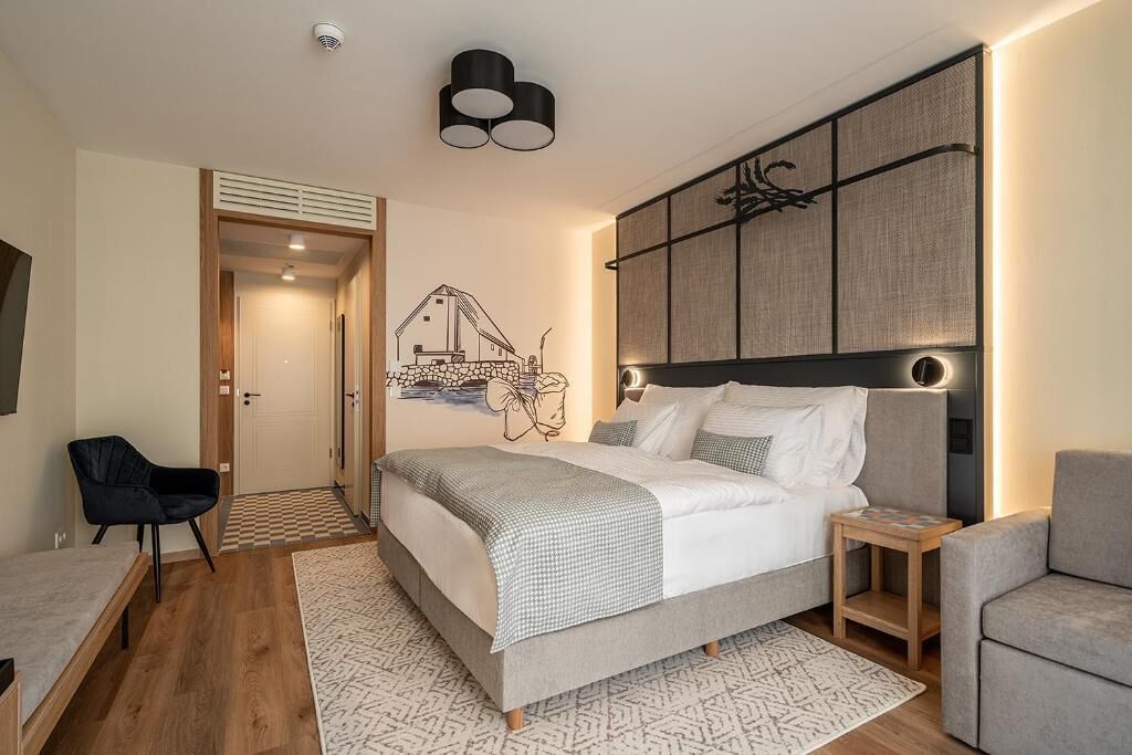 A modern bedroom with a bed, bedside tables, a chair, and a wall-mounted artwork.