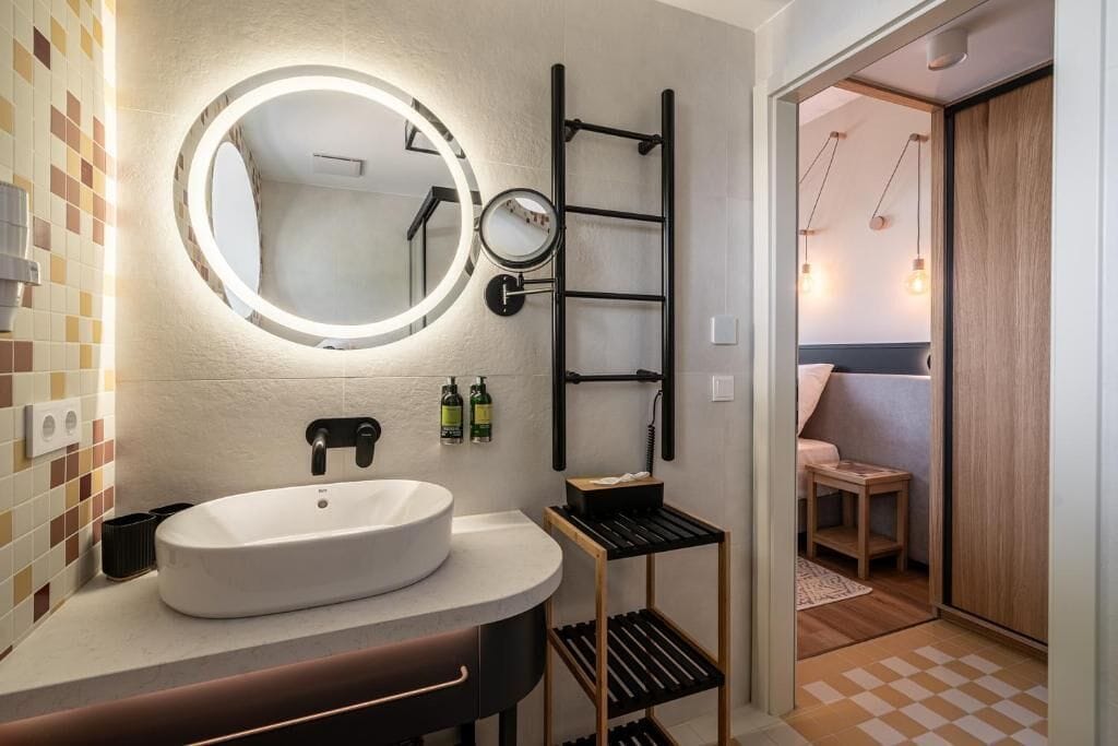 Un baño moderno con un espejo redondo, un lavamanos blanco y un perchero negro.