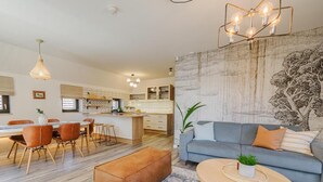 A modern living room with a sofa, coffee table, and ottoman. There is a dining area with chairs and a table. A kitchen is visible in the background. - Malom és Kacsa Boutique Hotel (Tata)