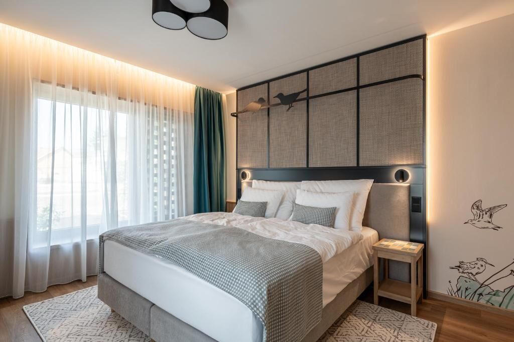 A modern bedroom with a large bed, a bedside table, and a headboard with a bird mural.