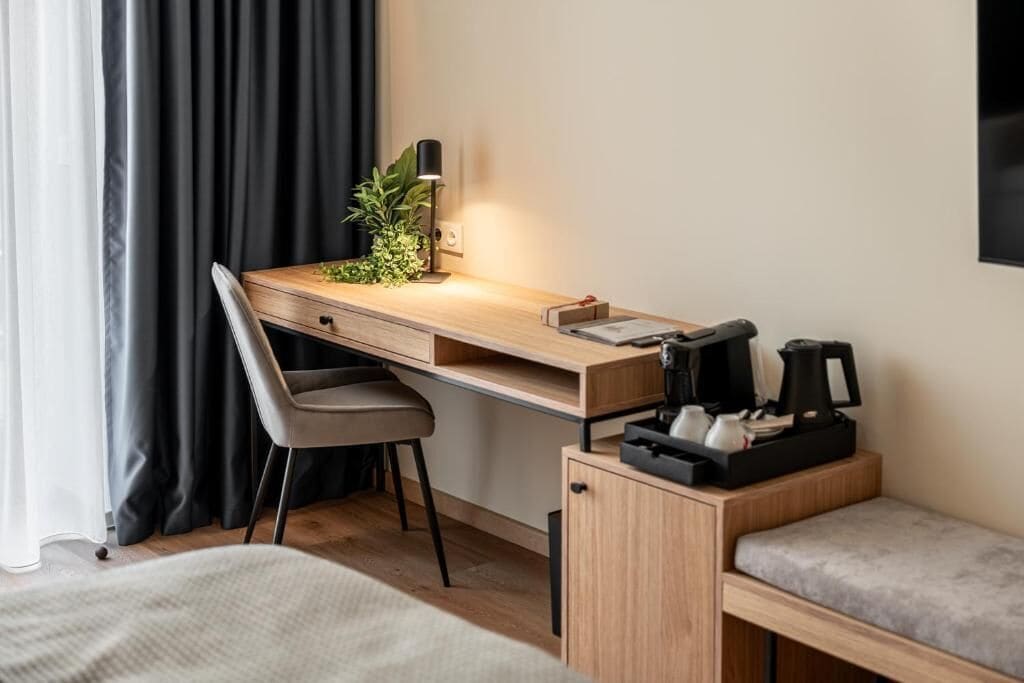 Et moderne hotelværelse med et træskrivebord, en stol, et lille skab og en bænk.