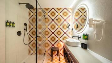Un baño con ducha, lavabo, espejo y un taburete.
