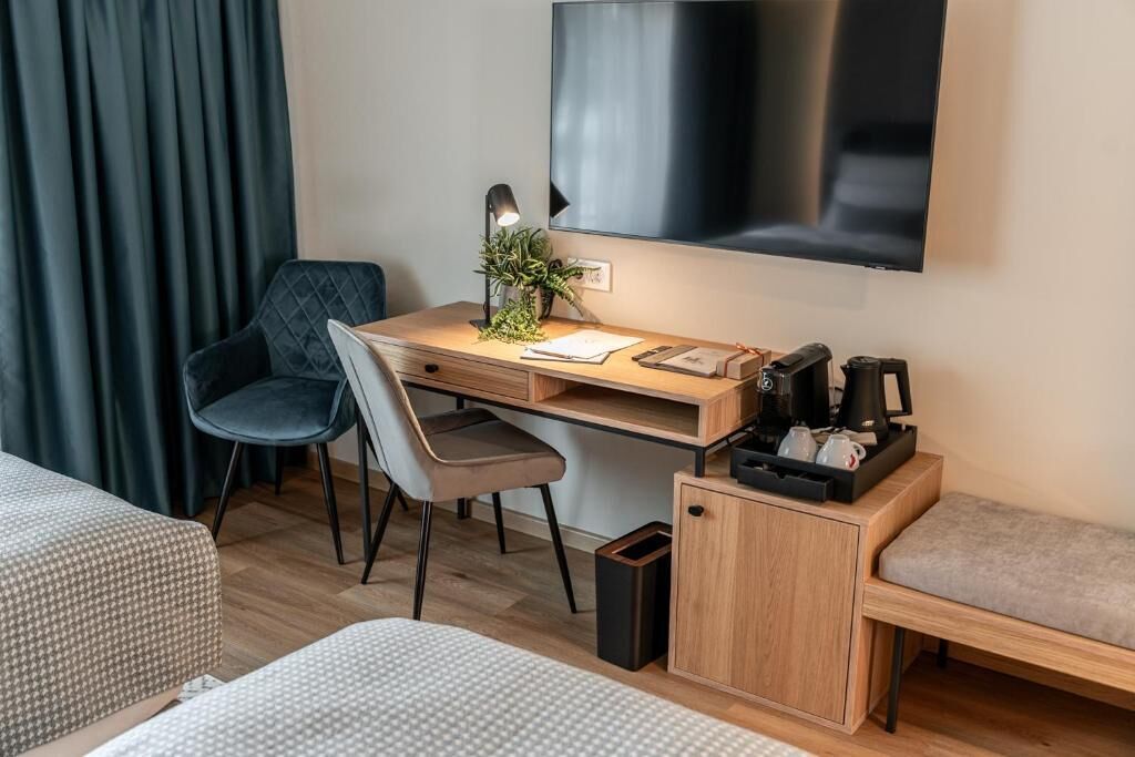A hotel room with a bed, a desk with a computer, a chair, a TV, and a small cabinet.