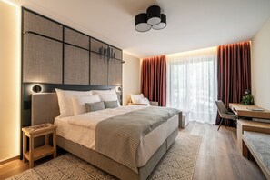 Une chambre à coucher moderne avec un grand lit, des tables de chevet, un bureau et une vue sur l’extérieur.