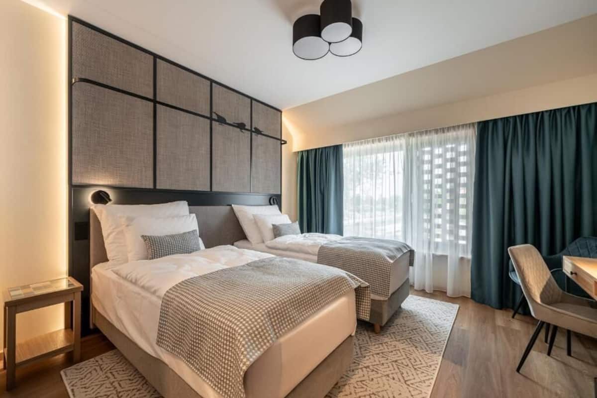 A modern hotel room with two beds, a desk, and a chair.