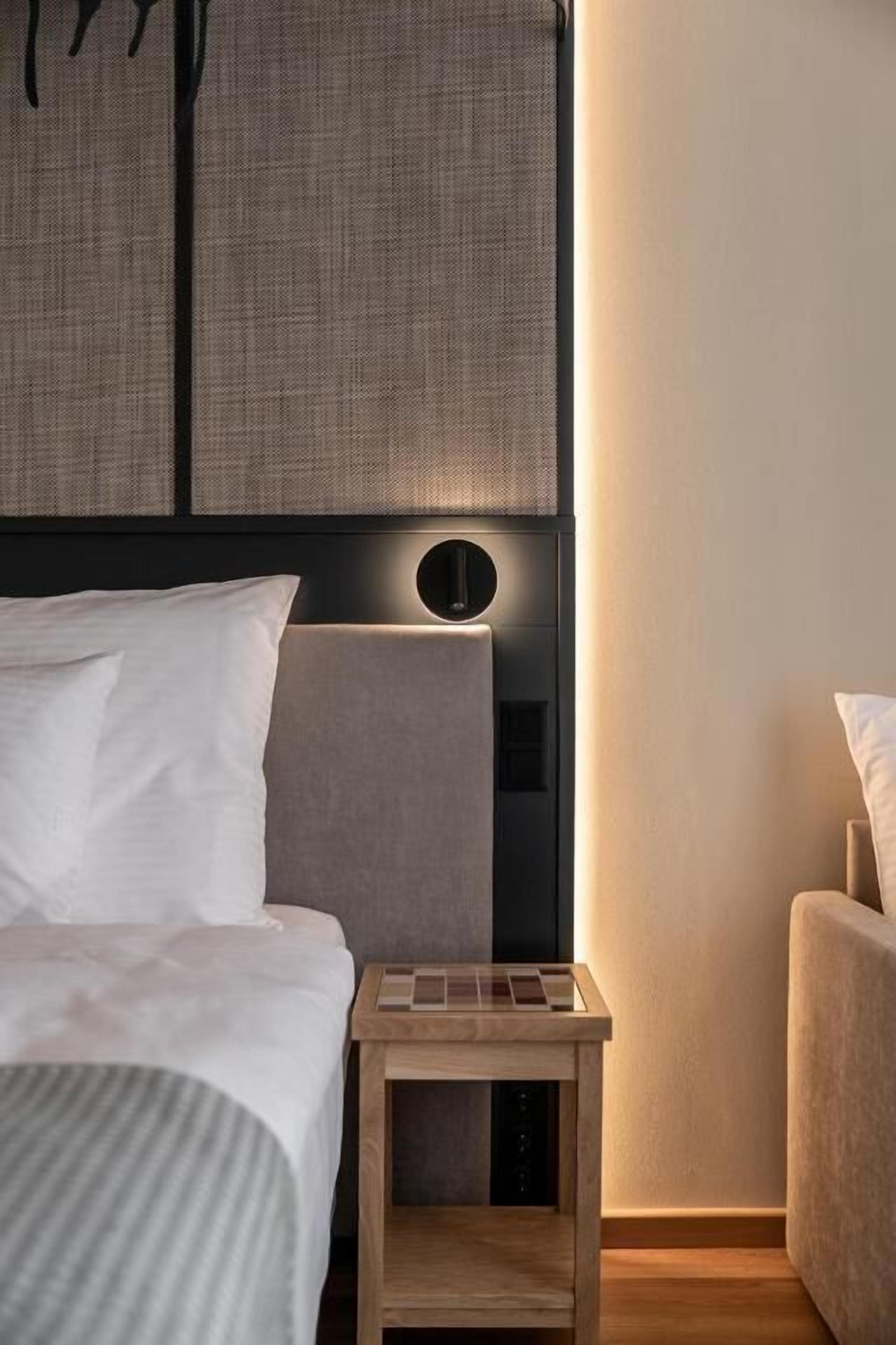 Quarto moderno com cama, mesa de cabeceira e luminária na parede.
