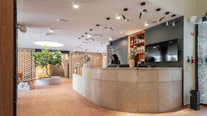 A reception area with a curved counter, a receptionist, a potted plant, and a brick wall. - Malom és Kacsa Boutique Hotel (Tata)