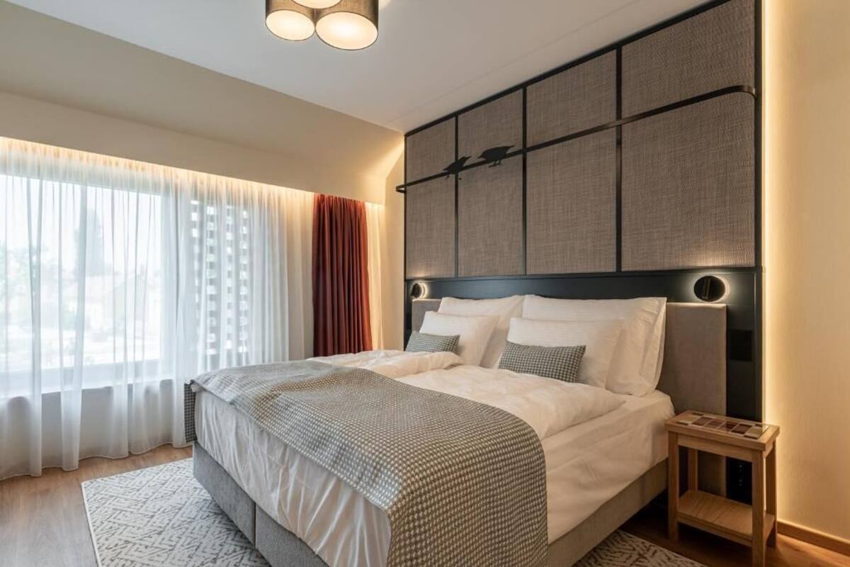 A modern bedroom with a large bed, a headboard with a bird design, and a bedside table with a clock.