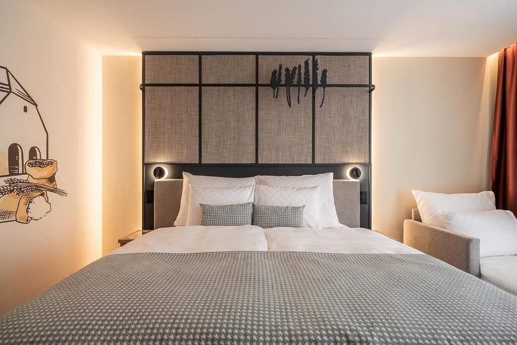 A hotel room with a large bed, a headboard with a textured panel, and a wall-mounted artwork.