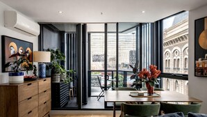 Un intérieur moderne comprenant un coin repas, un canapé et une vue sur le paysage urbain grâce à de grandes fenêtres.