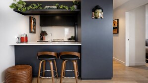 Une cuisine moderne avec un mur de couleur sombre, deux tabourets de bar en bois, un petit tabouret rond en bois et une statue de Bouddha.