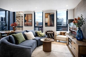 A modern living room with a sectional sofa, a round coffee table, a side table, and a television. - StayCentral - The Harmony @ Collingwood - Robert St, Collingwood - 2 bedrooms, 2 Beds, 1 Bathroom, 1 Parking (Collingwood)