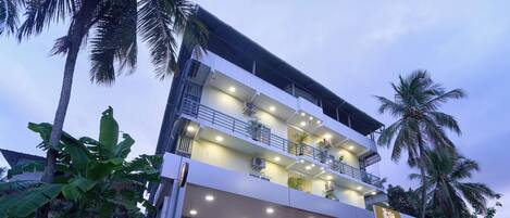 A multi-story hotel with balconies, air conditioning units, and a well-lit entrance.