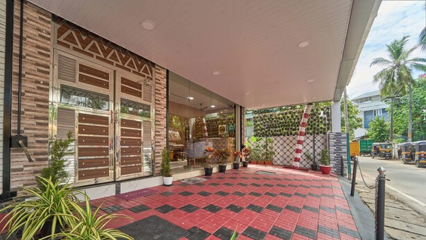 Entrada de hotel con piso a cuadros rojo y negro, plantas en macetas y una zona techada con pared decorada.