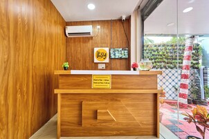 Un mostrador de recepción de madera con un cartel que indica horarios de registro de entrada y salida, un televisor montado y una pared de plantas en macetas.