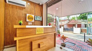A hotel reception desk with a wooden finish, a sign indicating check-in/out times, and a view of the street outside.