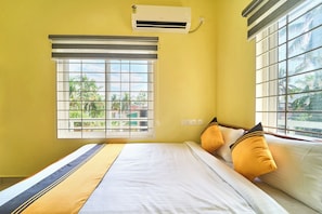 A room with a bed, a window with blinds, an air conditioning unit, and a view of greenery outside. - Itsy Hotels Salees Enclave - Near Padmanabhaswamy Temple (Thiruvananthapuram)