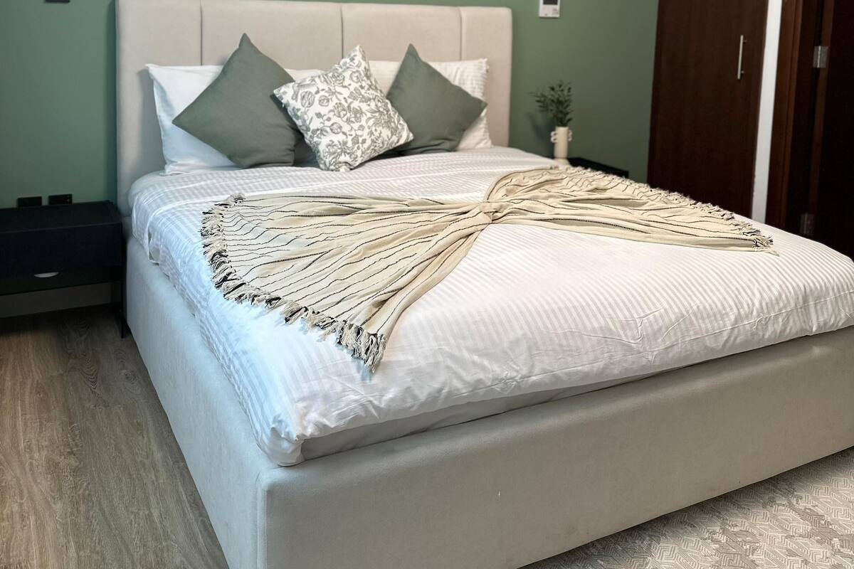 A bedroom with a bed, a nightstand, a dresser, and a door.