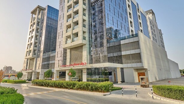 A modern multi-story hotel with a glass facade, a central entrance, and a landscaped driveway.