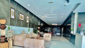 A modern lobby with a sofa, armchairs, a reception desk, and framed artwork on the wall.