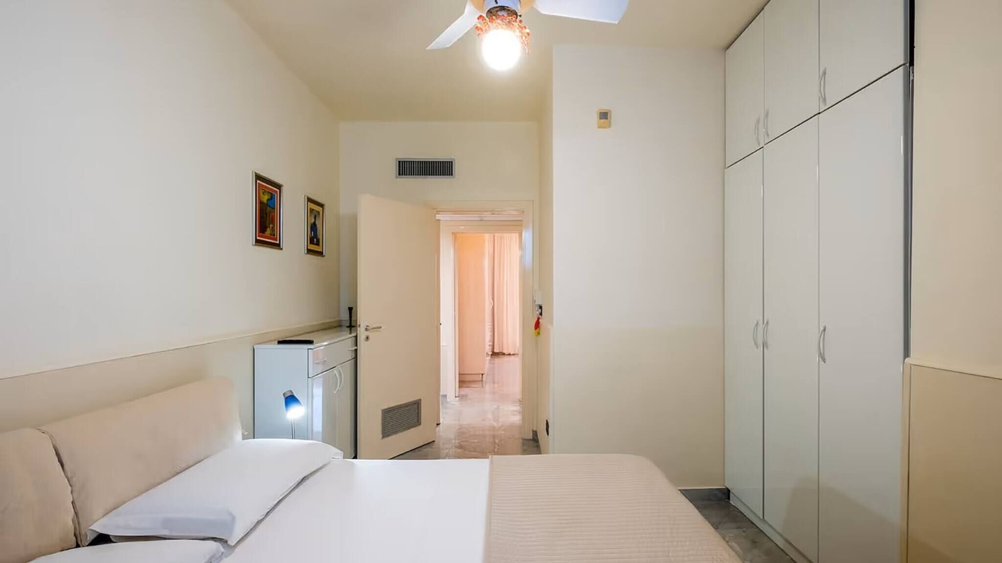 A narrow hotel room with a bed, a desk, and a wardrobe.