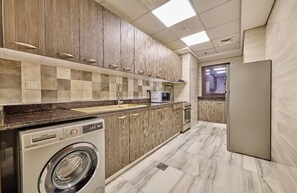 A modern kitchen with wooden cabinets, a built-in oven, a microwave, and a washing machine. - Grand Stay Holiday Homes Rental Al Jadaf (Dubai)