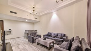 Ein geräumiges Wohnzimmer mit Marmorboden, grauen Sofas, einem Couchtisch und einer Chandelier.