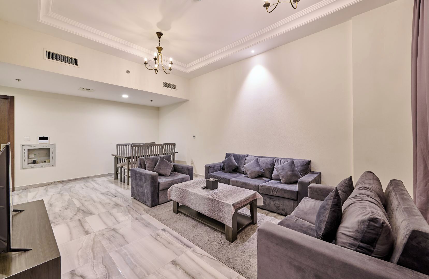 A spacious living room with a marble floor, grey sofas, a coffee table, and a chandelier.