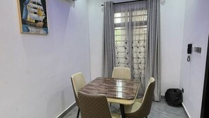 Un comedor con una mesa rectangular y cuatro sillas, un cuadro en la pared, una ventana con cortinas y un teléfono en la pared.