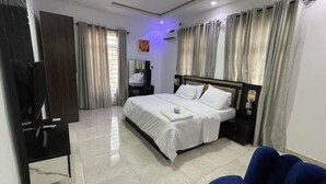 Un dormitorio con cama, televisor, escritorio y cortinas.