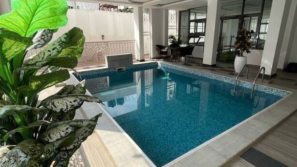 Una piscina interior con agua azul cristalina, rodeada de piso de baldosas y pared blanca.