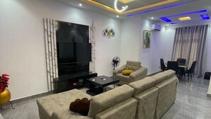 Una sala moderna con un televisor de pantalla plana grande, un sofá, una mesa de centro y un comedor con mesa y sillas.
