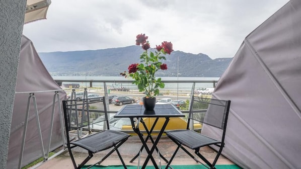 A balcony with a table and chairs, a potted plant, and a view of a body of water and mountains. - HOTEL DU POÈTE (Tresserve)
