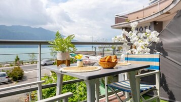 A balcony with a table set for breakfast, overlooking a body of water and mountains.