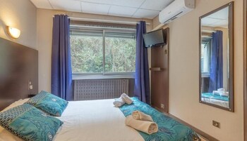 A hotel room with a bed, a large window with curtains, a flat-screen TV, and a mirror on the wall.