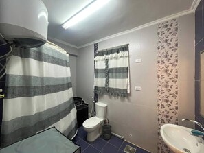 Une salle de bain équipée de toilettes, d’un lavabo, d’un rideau de douche et d’une fenêtre également dotée d’un rideau.