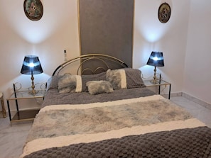Un lit bien fait, recouvert d’une couverture grise et blanche, avec deux lampes de chevet de chaque côté, posées sur des supports métalliques assortis.
