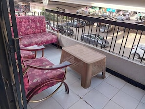 Un balcon avec un ensemble de meubles de salon comprenant un canapé et une petite table, donnant sur une rue animée où sont garées des voitures.