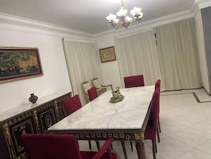 Une salle à manger avec une table en marbre, des chaises rouges, un lustre et des rideaux.