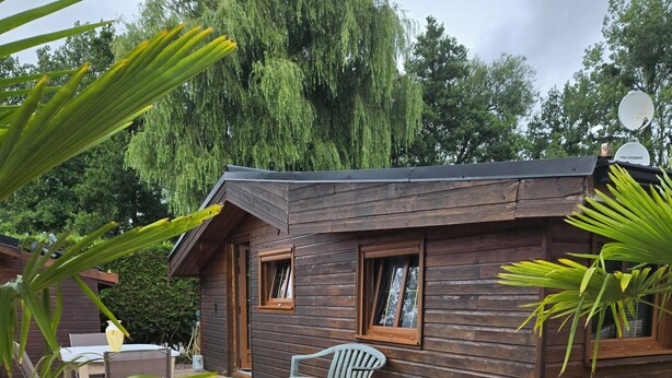 Eine Holzhütte mit einer Terrasse, zwei Fenstern und einem Stuhl.