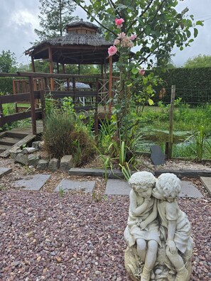 A garden with a gazebo, a rose bush, and a stone sculpture of two figures.