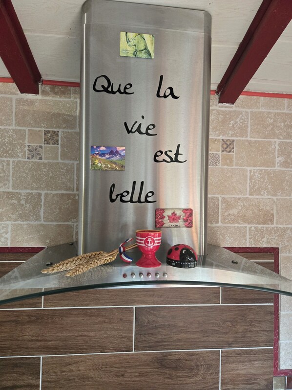 A stainless steel range hood with a French phrase written on it, a small Canadian flag, and a ladybug decoration.