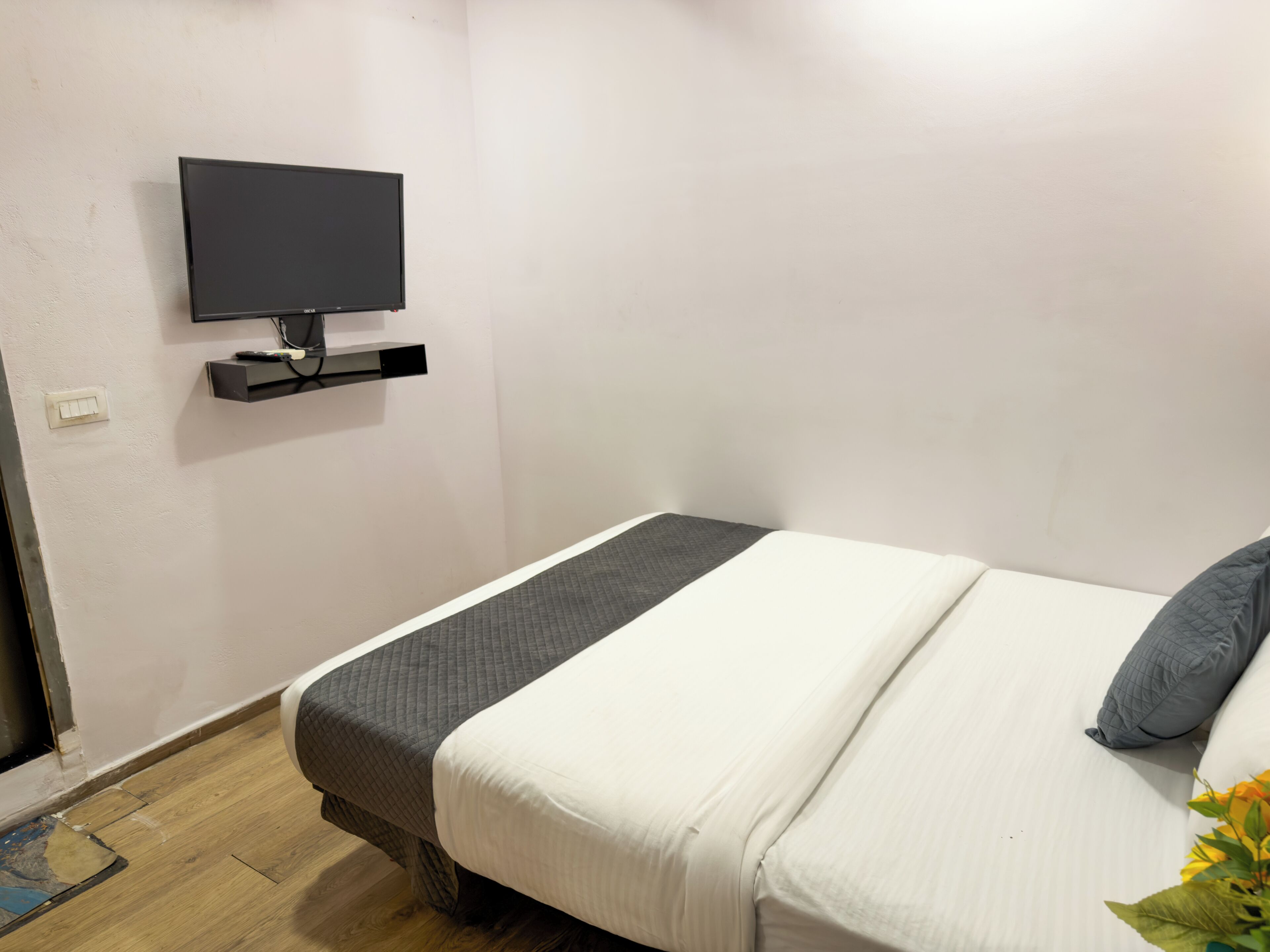 A hotel room with a bed, a TV mounted on the wall, and a wooden floor.