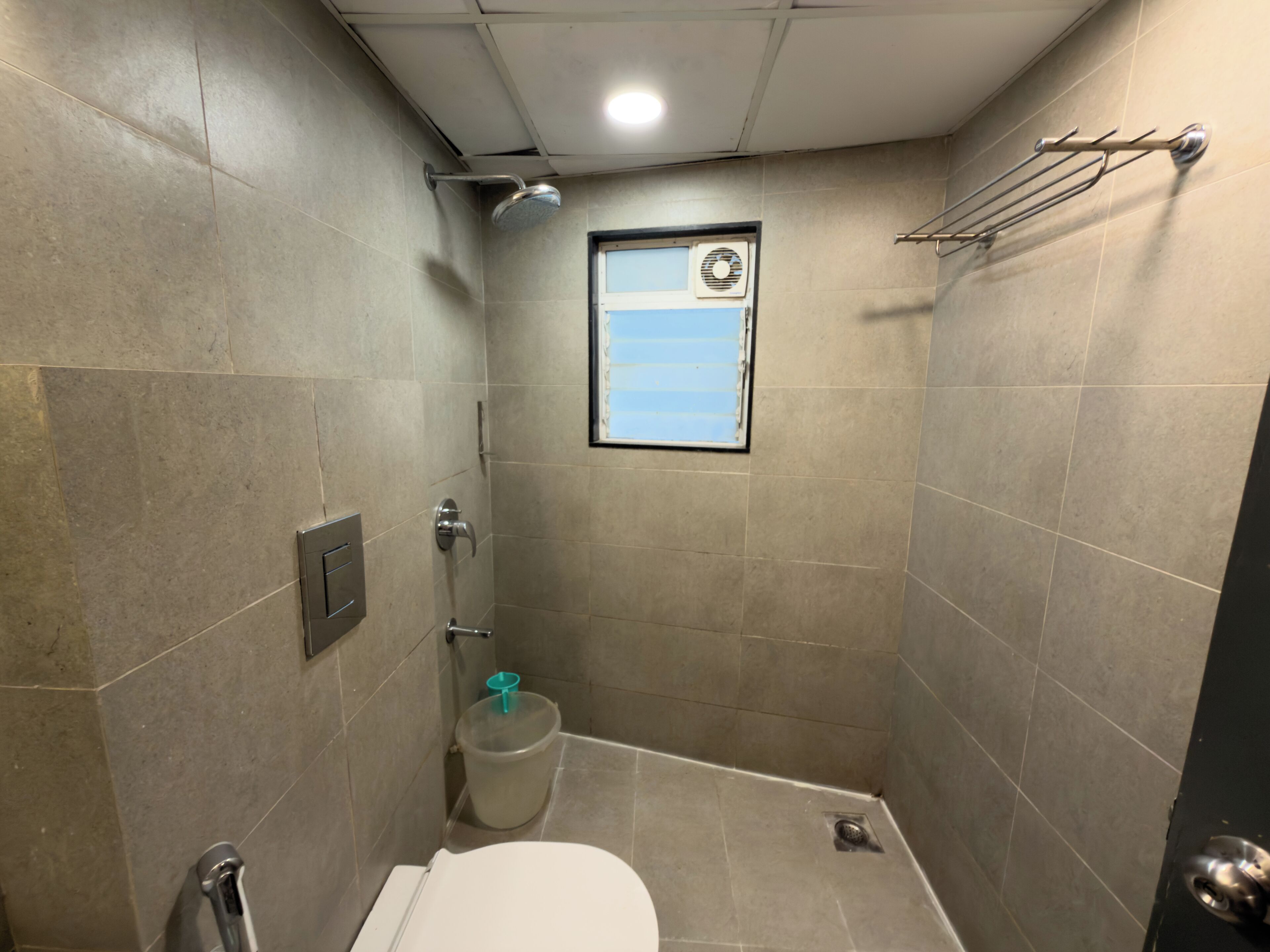 A small, tiled bathroom with a shower, toilet, and a window.