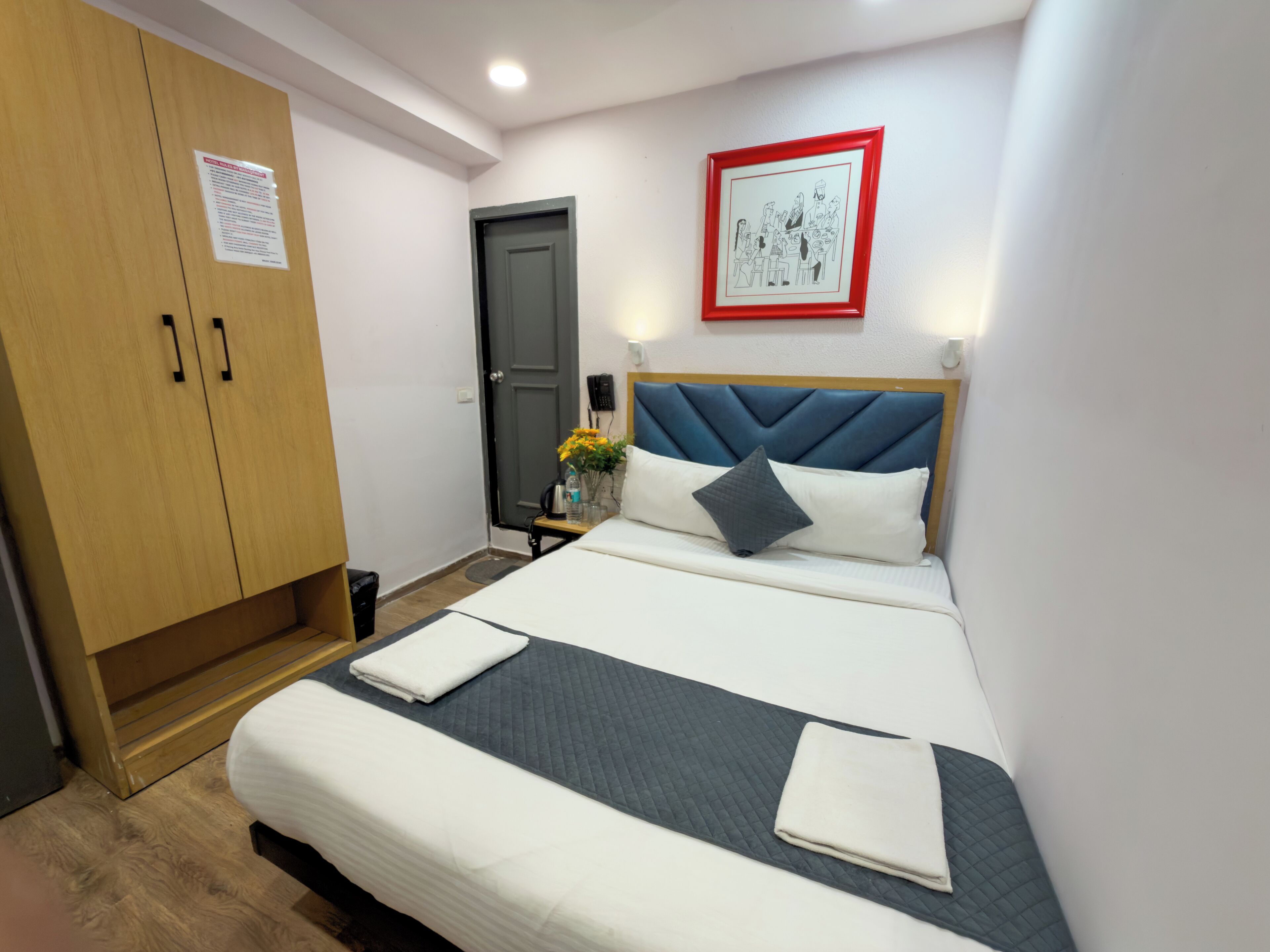 Une chambre d’hôtel avec un lit, une armoire, un tableau encadré au mur et une porte.