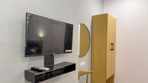 Ein modernes Zimmer mit einem an der Wand befestigten Fernseher, einem Holzschrank, einem Spiegel und einem kleinen Holzstuhl.