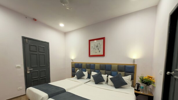 Ein Hotelzimmer mit zwei Betten, einem hölzernen Kopfteil, einem gerahmten Bild an der Wand und einem Nachttisch mit Blumen.