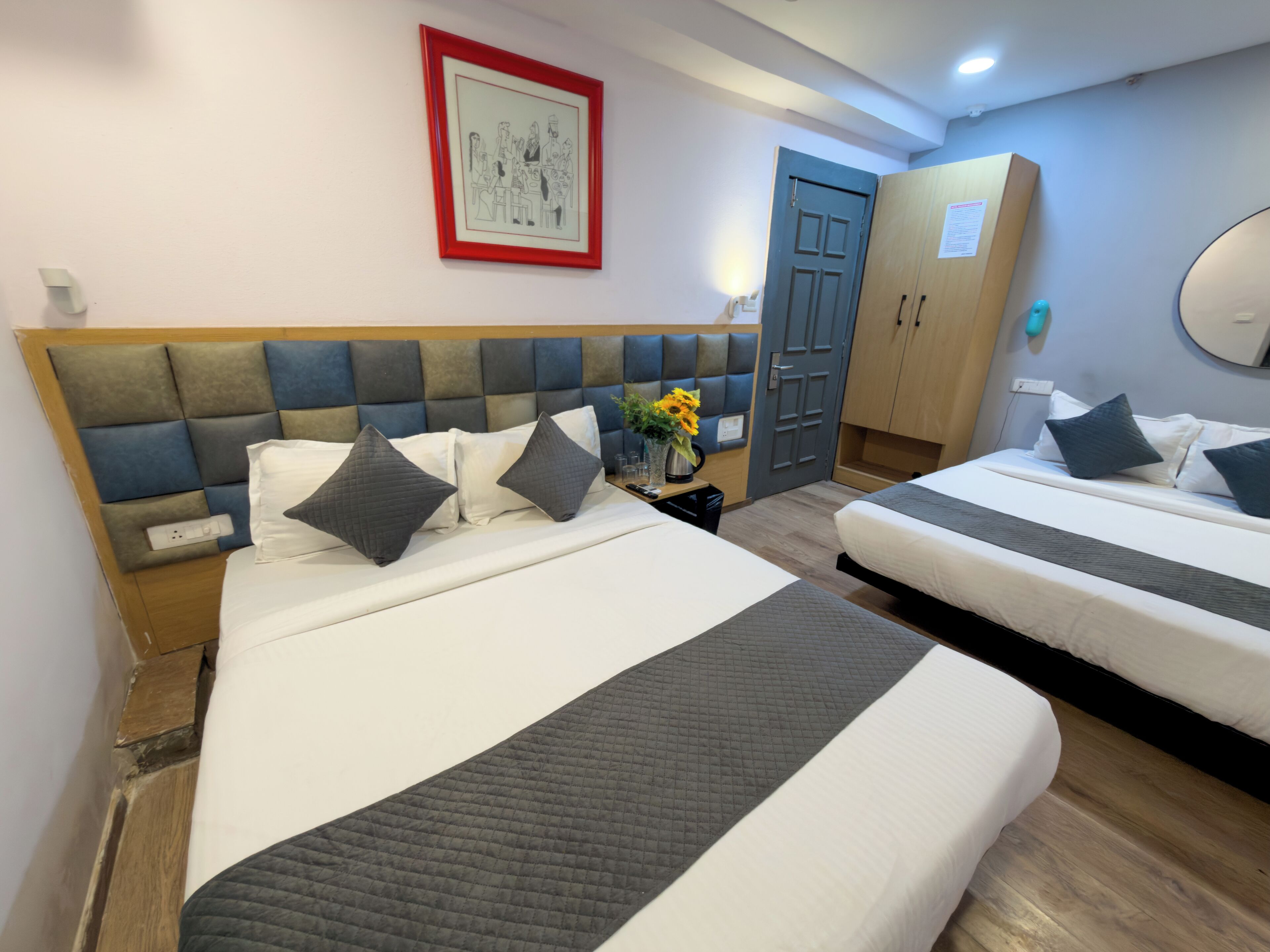 A hotel room with two beds, a headboard, a framed picture on the wall, a door, and a mirror.