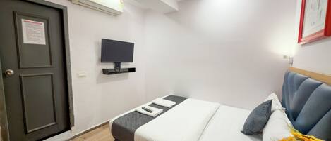 A hotel room with a bed, a TV mounted on the wall, a door, and an air conditioning unit.